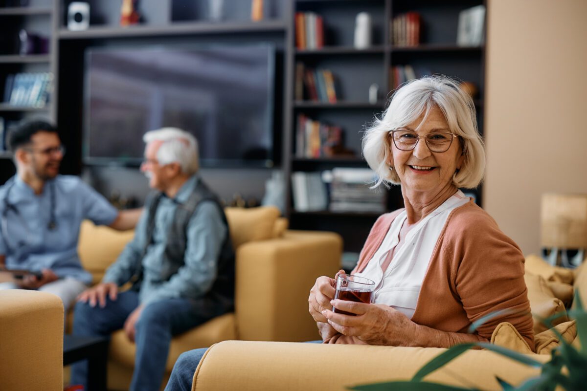 Happy senior woman drinking tea at residential care home and looking at camera.