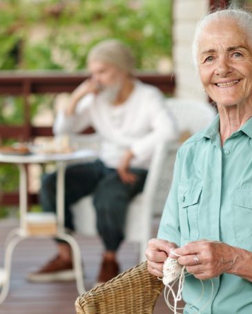 Cheerful senior woman with white hair looking at camera while knitting